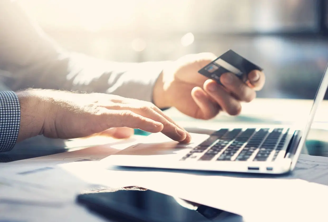 A person holding a credit card while using a laptop.